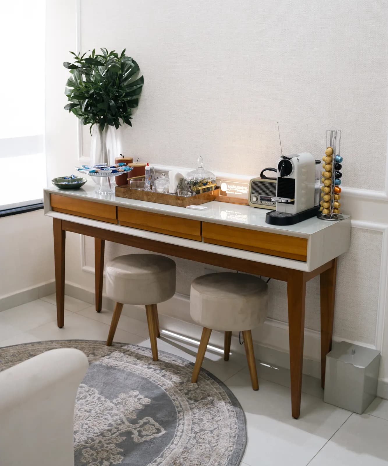 Recepção do consultório da psicóloga Denise Donda, com mesa de entrada, banquinhos redondos de veludo bege e um vaso com folhagem verde